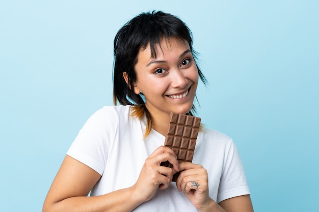 Jeune femme sur bleu isolé prenant une tablette de chocolat et heureux