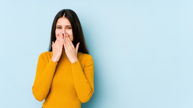 Jeune femme sur bleu rire de quelque chose, couvrant la bouche avec les mains.