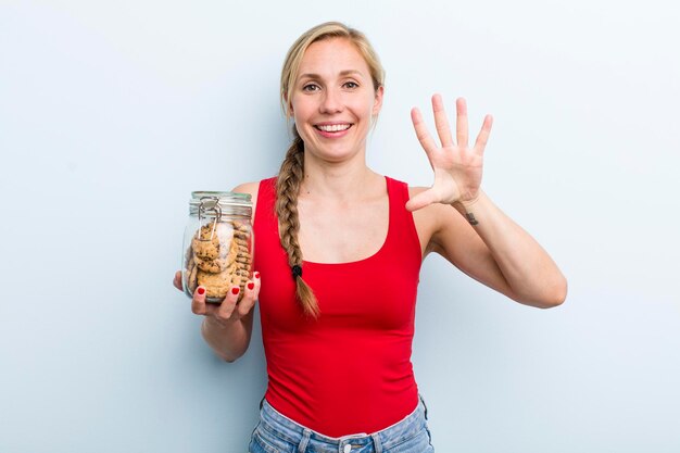 Jeune femme blonde adulte avec une bouteille de biscuits faits maison