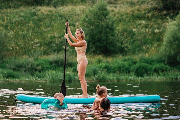 Jeune femme blonde adulte en maillot de bain jaune aviron avec aviron debout à bord naviguant sur la rivière tout en