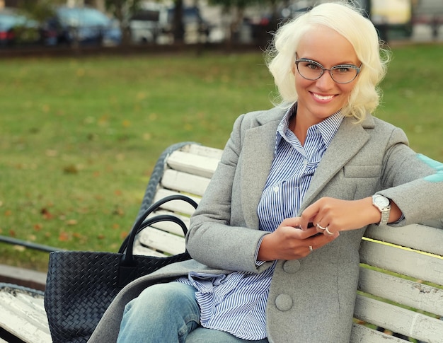 Jeune femme blonde à l'aide d'un téléphone intelligent à l'extérieur de la journée d'automne