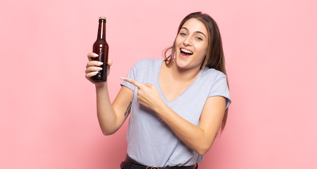 Jeune femme blonde à l'air excitée et surprise pointant vers le côté et vers le haut pour copier l'espace