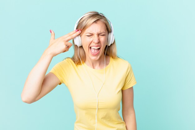 Jeune femme blonde à l'air malheureuse et stressée, geste de suicide faisant un signe d'arme à feu et écoutant de la musique.