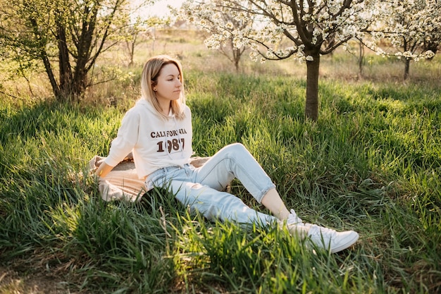 Jeune femme blonde assise sur l'herbe dans le parc à la lumière du soleil