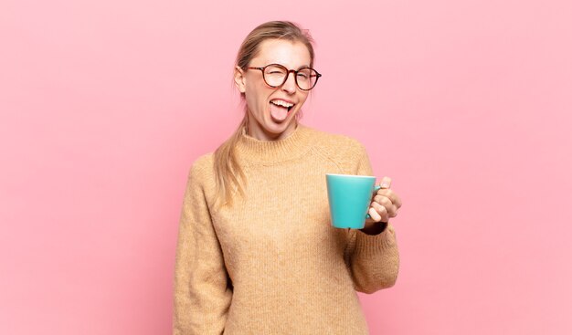 Jeune femme blonde à l'attitude joyeuse, insouciante et rebelle, plaisantant et tirant la langue, s'amusant. concept de café