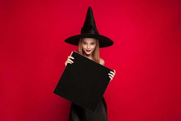 Jeune femme blonde au chapeau noir et costume sur fond rouge