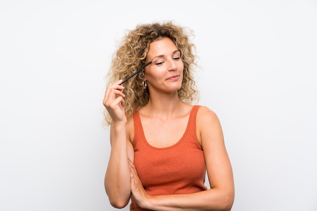 Jeune femme blonde aux cheveux bouclés, application de mascara à la ruée cosmétique