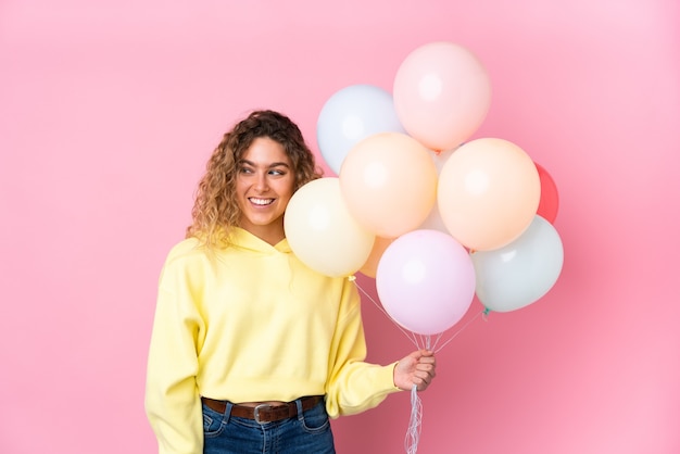 Jeune femme blonde aux cheveux bouclés attraper de nombreux ballons debout et regardant sur le côté