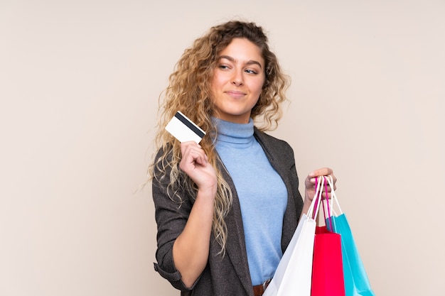 Jeune femme blonde aux cheveux bouclés isolé sur beige tenant des sacs et une carte de crédit