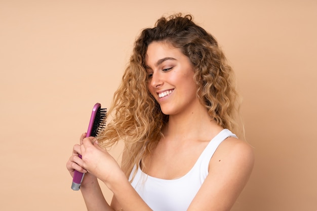 Jeune femme blonde aux cheveux bouclés sur mur beige avec peigne à cheveux