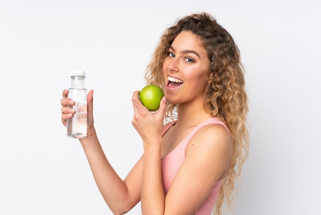 Jeune femme blonde aux cheveux bouclés sur mur blanc avec une pomme et avec une bouteille d'eau