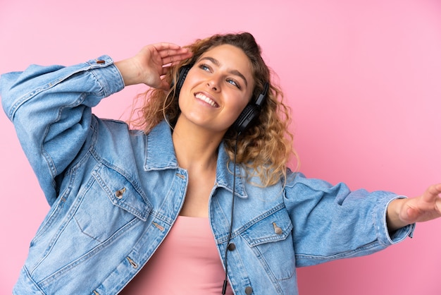 Jeune femme blonde aux cheveux bouclés sur le mur rose, écouter de la musique et danser