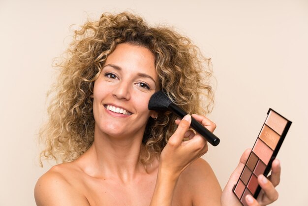 Jeune femme blonde aux cheveux bouclés avec un pinceau de maquillage