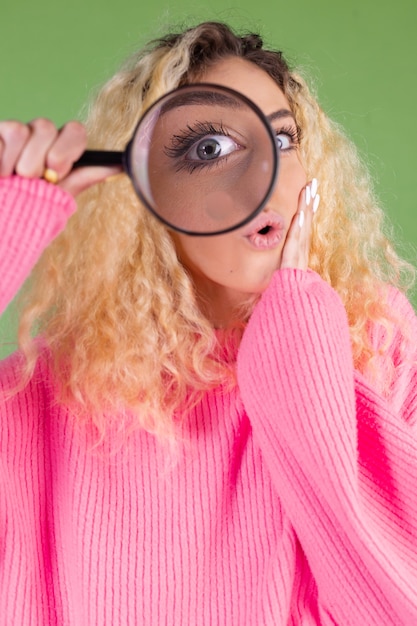 Photo jeune femme blonde aux longs cheveux bouclés en pull rose sur vert avec loupe choqué surpris