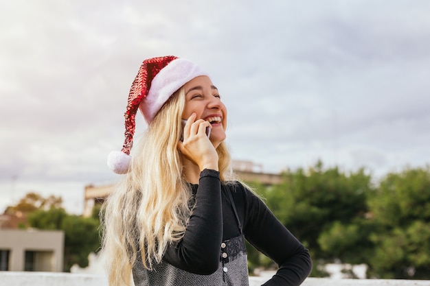 Jeune femme blonde ayant un appel téléphonique de Noël en riant et en s'amusant. Concept de Noël et de communication