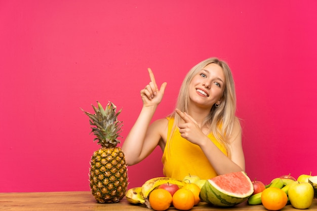 Jeune femme blonde avec beaucoup de fruits montrant avec l'index une excellente idée