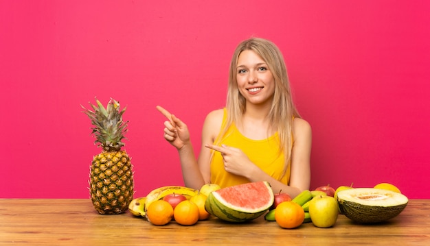 Jeune femme blonde avec beaucoup de fruits, pointant le doigt sur le côté