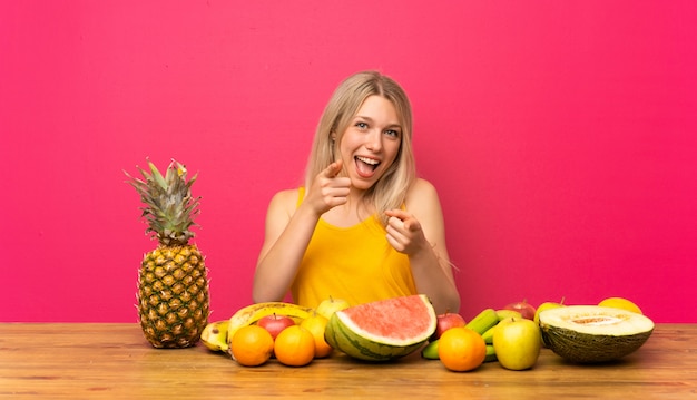 Jeune femme blonde avec beaucoup de fruits pointe vers vous