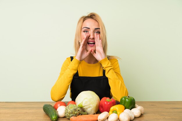 Jeune femme blonde avec beaucoup de légumes crier avec la bouche grande ouverte