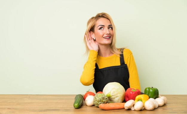 Jeune femme blonde avec beaucoup de légumes écoute quelque chose