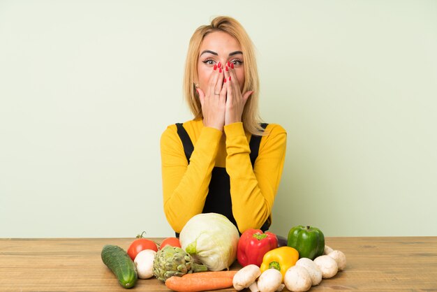 Jeune femme blonde avec beaucoup de légumes avec une expression faciale surprise