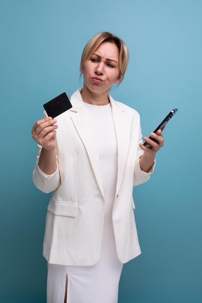 Jeune femme blonde bien soignée dans une veste et une robe blanches montre une carte bancaire en plastique