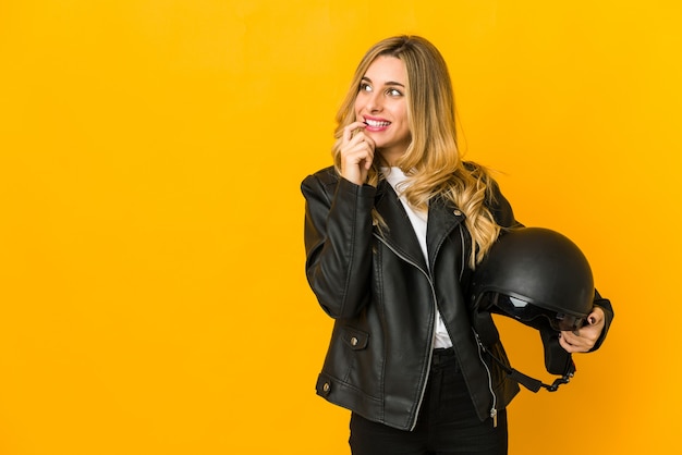 Jeune femme blonde biker caucasien tenant un casque détendu penser à quelque chose en regardant un espace de copie.