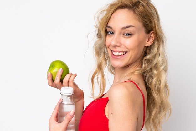 Jeune femme blonde sur blanc avec une pomme et avec une bouteille d'eau