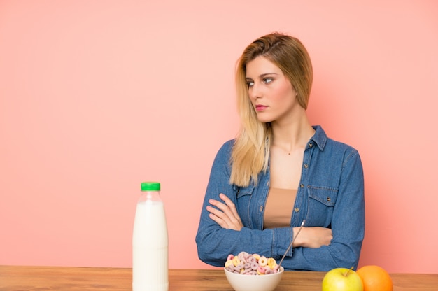 Jeune femme blonde avec bol de céréales debout et regardant à côté