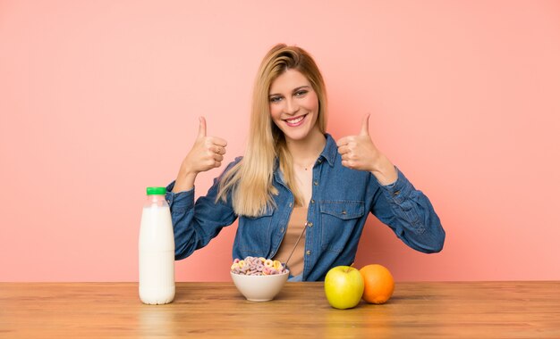 Jeune femme blonde avec bol de céréales donnant un geste du pouce levé