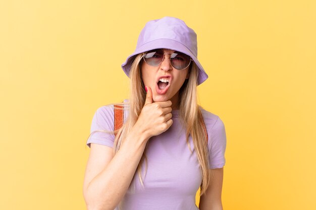 Jeune femme blonde avec la bouche et les yeux grands ouverts et la main sur le menton