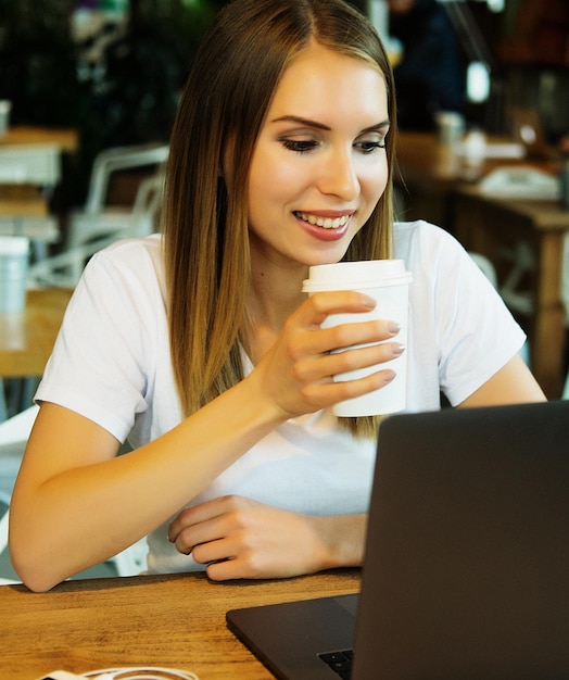 Jeune femme blonde buvant du café et utilisant un ordinateur portable dans un café