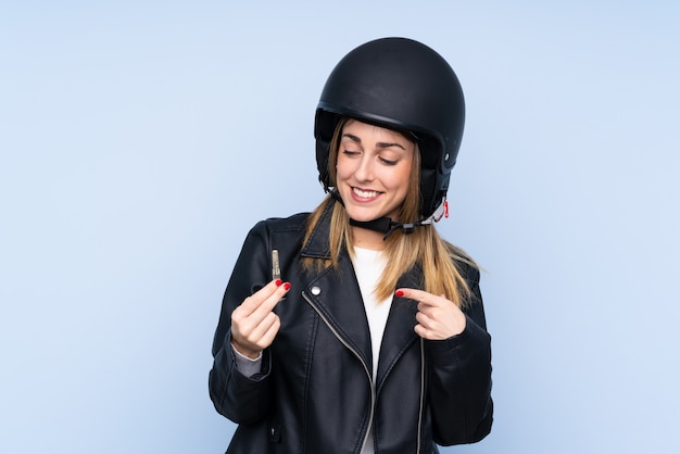 Jeune femme blonde avec un casque de moto et une clé sur le mur bleu isolé