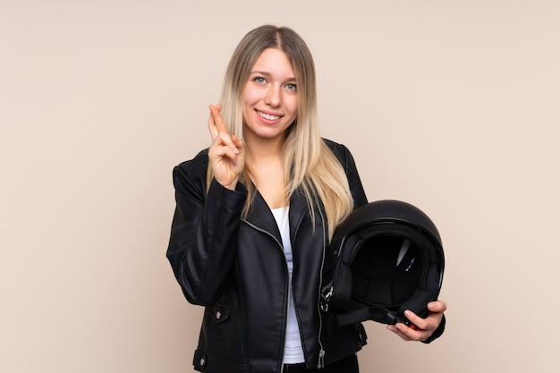 Jeune femme blonde avec un casque de moto sur un mur isolé avec les doigts traversant