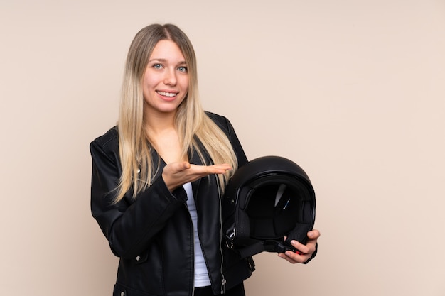 Jeune Femme Blonde Avec Un Casque De Moto Sur Un Mur Isolé, Tendant Les Mains Sur Le Côté Pour Inviter à Venir