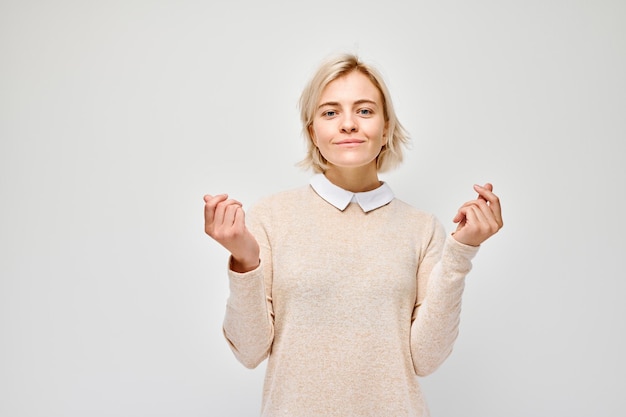 Jeune femme blonde en casual tenant quelque chose à la main démontrant un espace vide pour le produit ou le texte isolé sur un fond de studio blanc