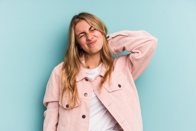 Jeune femme blonde caucasienne isolée sur fond bleu ayant une douleur au cou due au stress, en la massant et en la touchant avec la main.