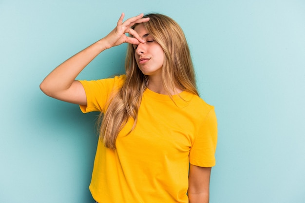 Jeune femme blonde caucasienne isolée sur fond bleu ayant mal à la tête, touchant le devant du visage.