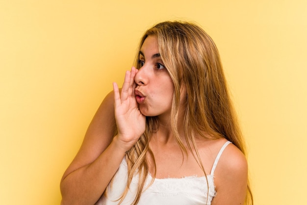 Jeune femme blonde caucasienne isolée sur fond jaune dit une nouvelle secrète de freinage à chaud et regarde de côté