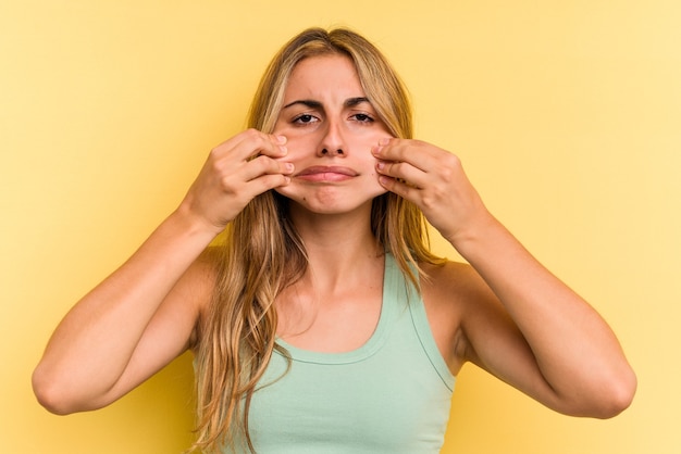 Jeune femme blonde caucasienne isolée sur fond jaune doutant entre deux options.