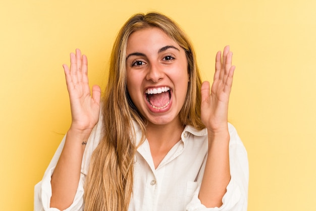 Jeune Femme Blonde Caucasienne Isolée Sur Fond Jaune Recevant Une Agréable Surprise, Excitée Et Levant Les Mains.