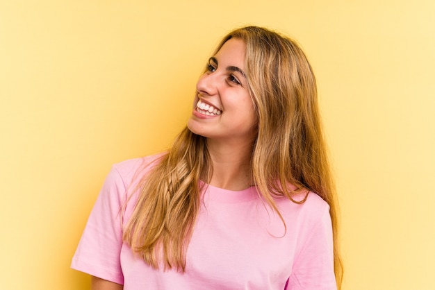 Jeune femme blonde caucasienne isolée sur fond jaune riant détendue et heureuse, cou tendu montrant les dents.