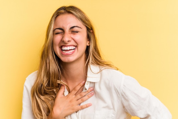 Jeune femme blonde caucasienne isolée sur fond jaune en riant en gardant les mains sur le cœur, concept de bonheur.