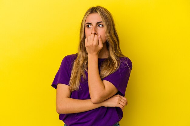 Jeune femme blonde caucasienne isolée sur fond jaune se rongeant les ongles, nerveuse et très anxieuse.