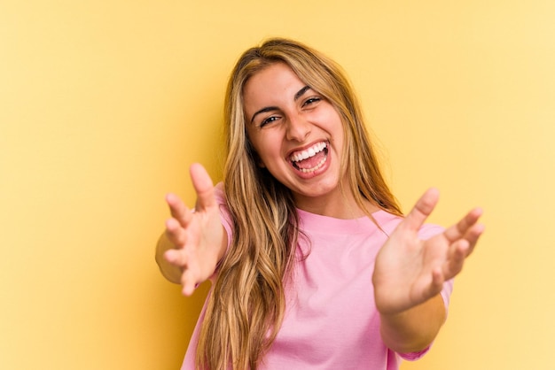 Jeune femme blonde caucasienne isolée sur fond jaune se sent confiante en donnant un câlin à la caméra.