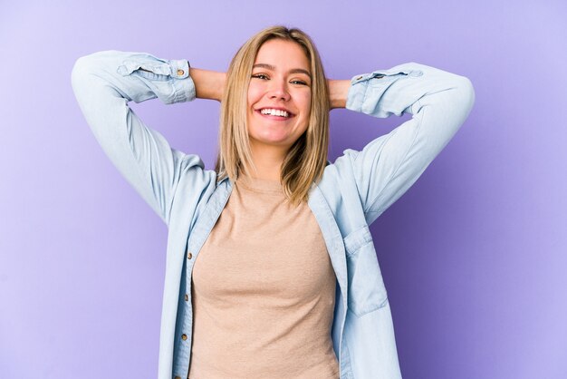 Jeune femme blonde caucasienne isolée se sentant confiant, avec les mains derrière la tête.