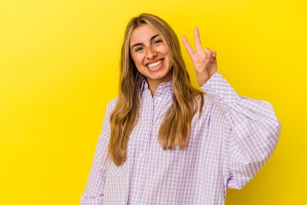 Jeune femme blonde caucasienne joyeuse et insouciante montrant un symbole de paix avec les doigts.