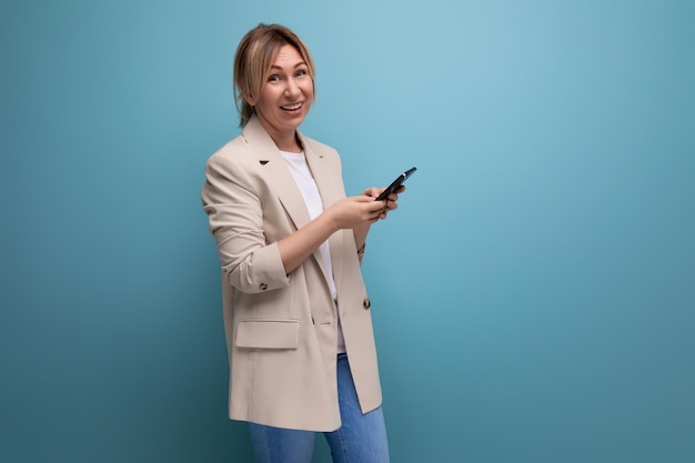 Jeune femme blonde chanceuse dans une veste avec un gadget dans ses mains sur un fond de studio
