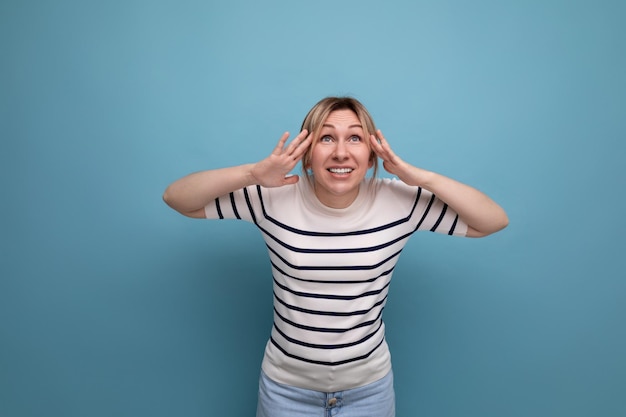 Une jeune femme blonde choquée dans un pull rayé est surprise sur un fond bleu avec espace de copie