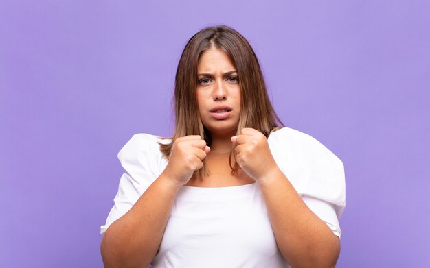 Jeune femme blonde à la confiance, en colère, forte et agressive, avec les poings prêts à se battre en position de boxe